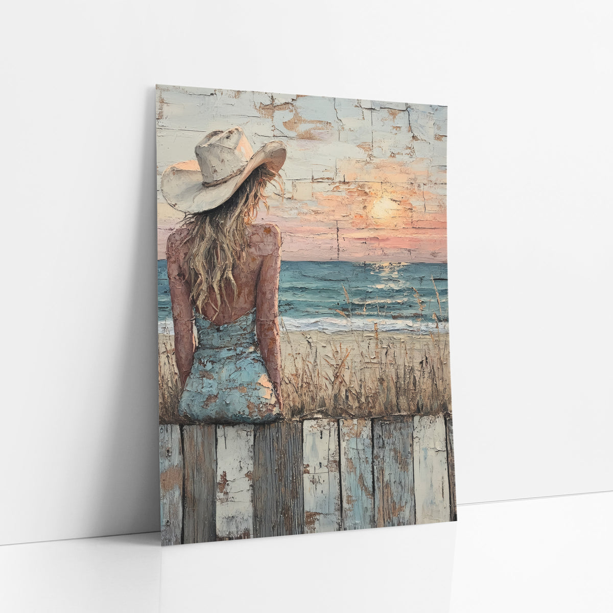 Cowgirl Watching Seaside Sunset Western art print leaning against a white wall – woman in a cream cowboy hat and blue dress